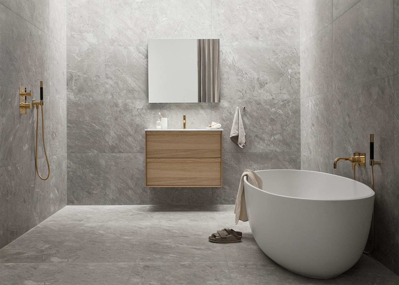 Modernt badrum med marmorbeklädda väggar, fritstående badkar och guldarmaturer